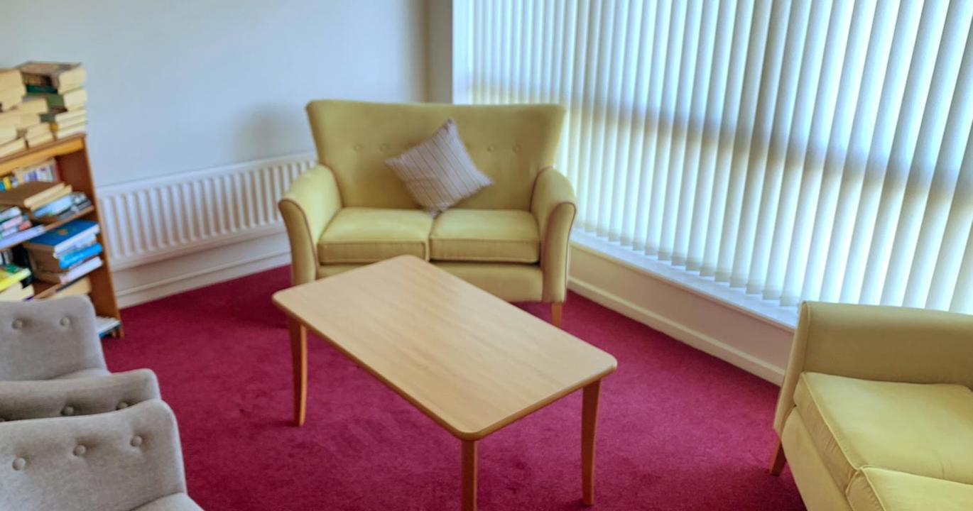 A cosy reading room with two small yellow sofas, a coffee table and a bookshelf filled with books