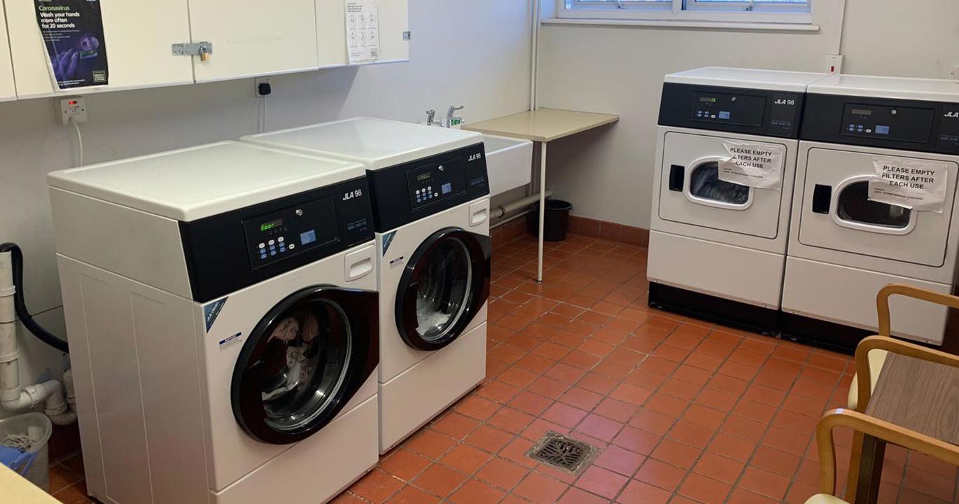 A laundry room with two large washing machines, two tumble driers and a sink