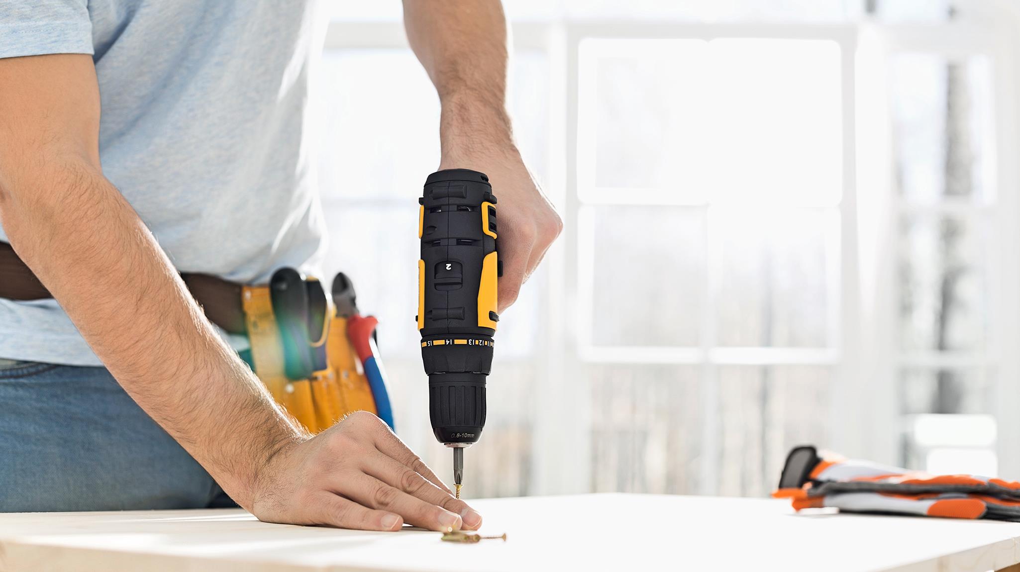 A close-up of a man's hand drilling into a table