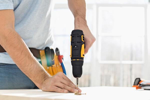 A close-up of a man's hand drilling into a table