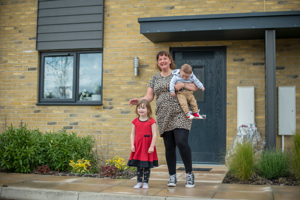 A woman and a child standing outside an Accent home smiling. She's holding a toddler in her arms 