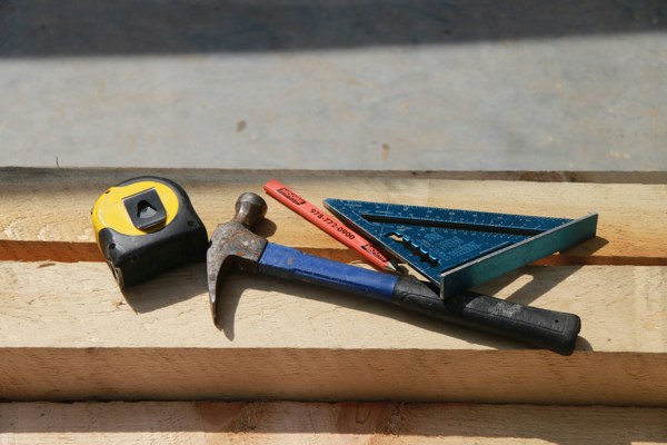 A tape measure, hammer, and other DIY goods resting on a plank of wood