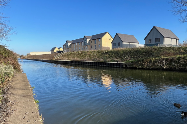 A canal on a sunny day, with a number of newly built homes on the far bank