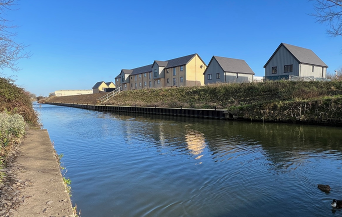 A canal on a sunny day, with a number of newly built homes on the far bank