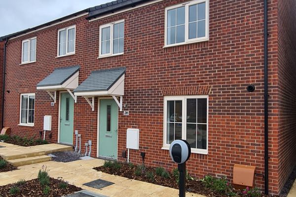 A two-storey red brick housing development with a sage-coloured front door and newly planted flower beds