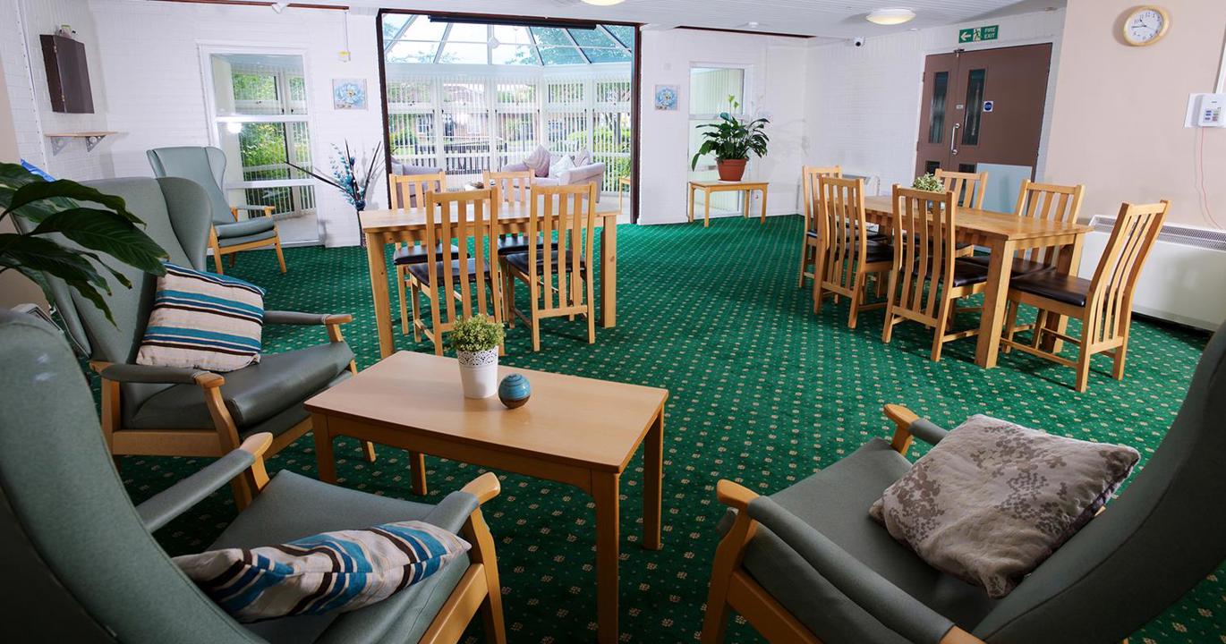 A comfortable reading room with chairs, tables, and a bright green carpet